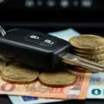 Alerta! Taxas de Juros de Financiamento de Carros Novos Podem Subir 2% Chave de carro sobre pilhas de moedas e notas, simbolizando o financiamento e as taxas de juros.
